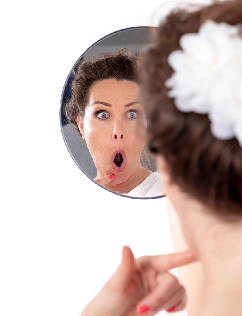Middle-aged doing facial exercises in the mirror - face yoga